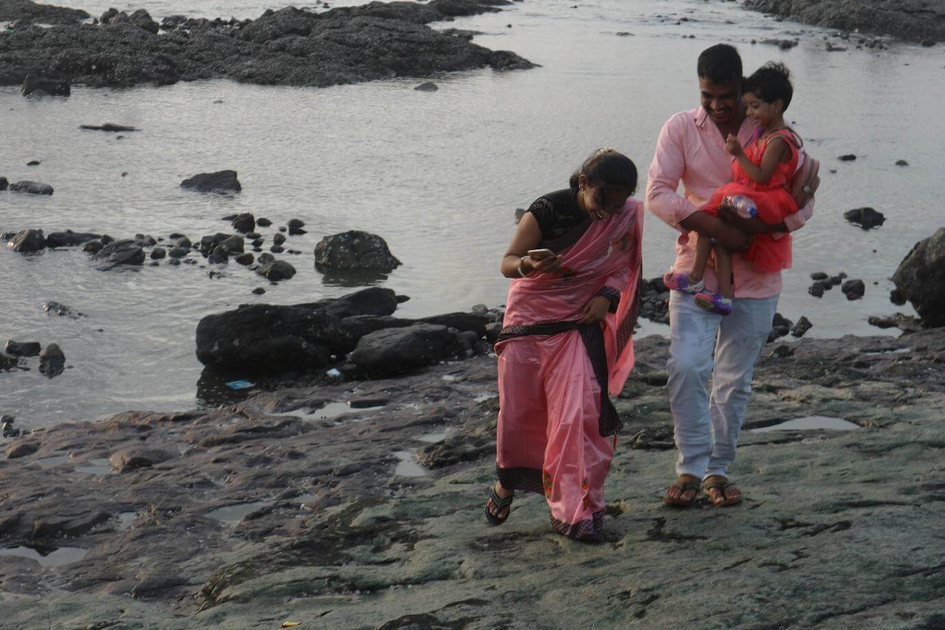 A family of three, a man, woman, and child, walk back to promenade, laughing. All three are wearing shades of pink.