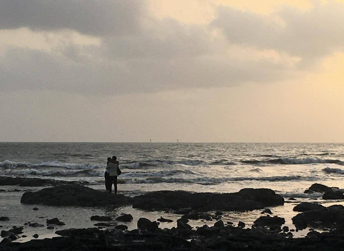A man and a woman kissing, locked in a tight embrace, standing on the rocks at Bandstand.