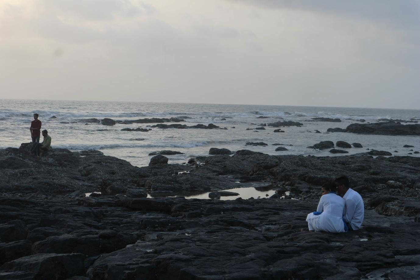 A man and woman (both dressed in white) whispering to each other while sitting on the rocks.