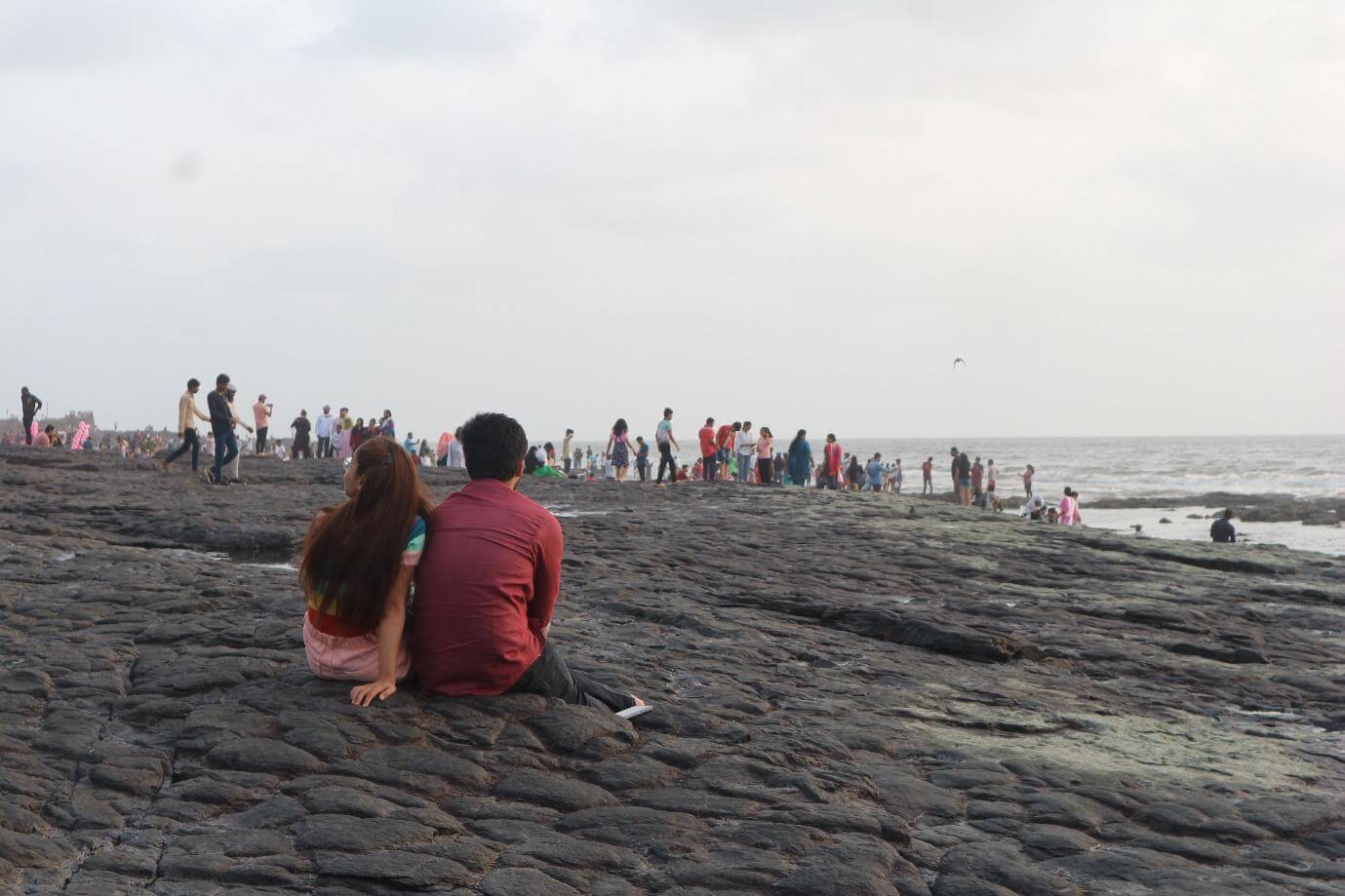 A woman and a man sit close to each other on the rocks, watching the people around them.