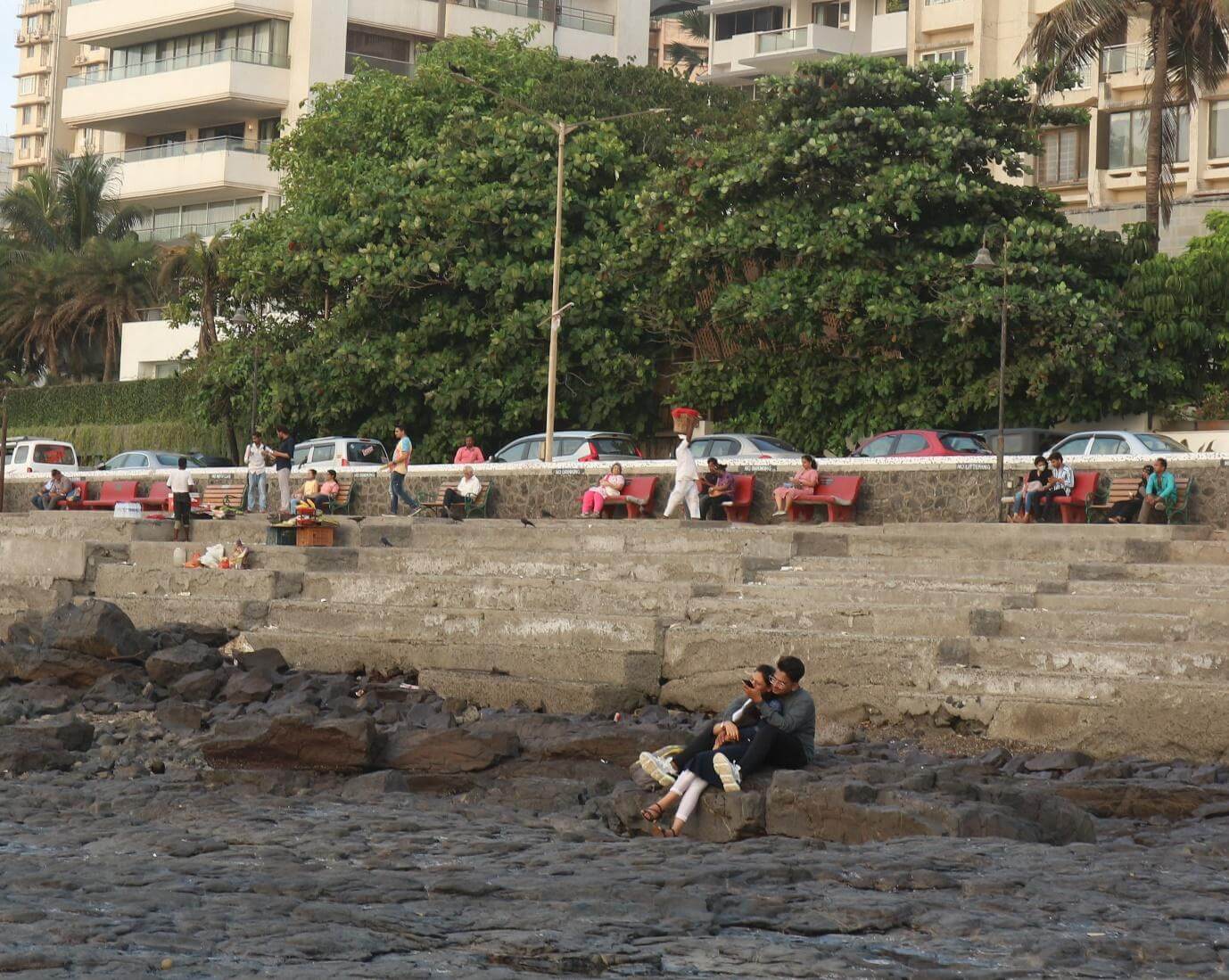A woman leans against a man, who is hugging her from behind, as they both sit on the rocks at Bandstand on a Saturday evening in May.