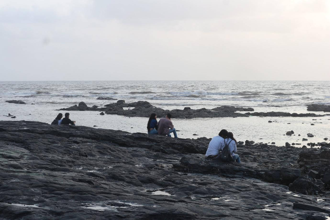 Three couples seated on the rocks, facing the sea at Bandstand.
