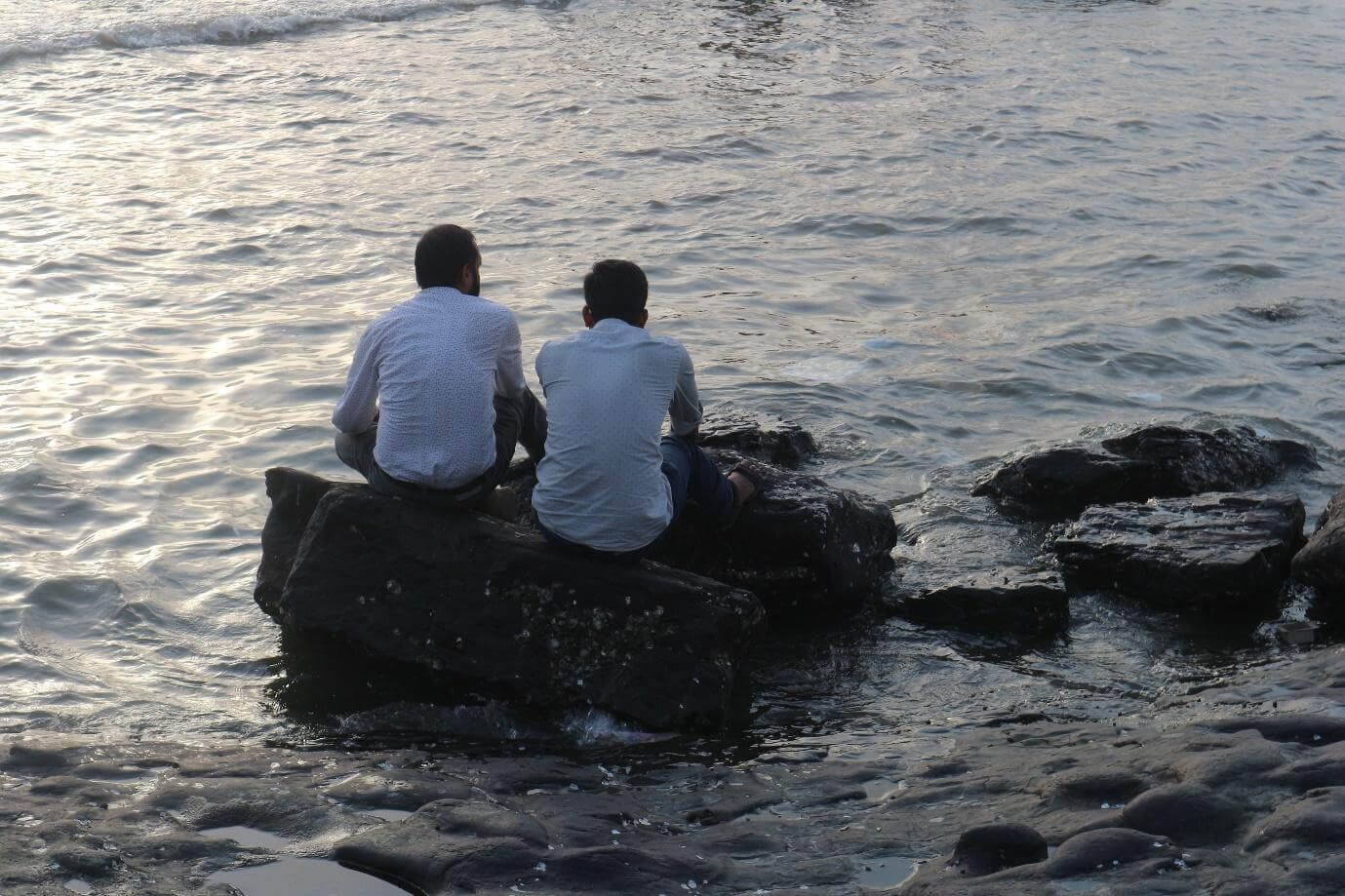 Two men sit close together at the edge of the rocks on Bandstand, contemplating the sea.